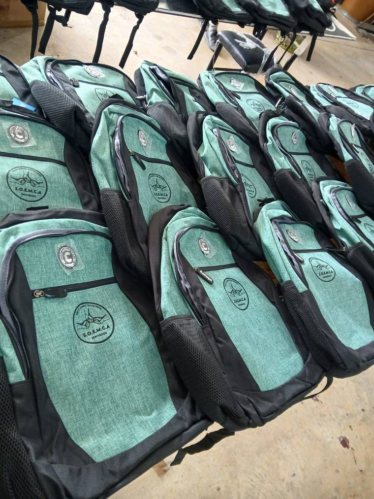 Mochilas verde agua con logo estampado, alineadas sobre una mesa del taller